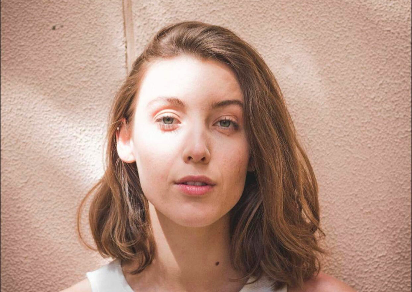 Headshot of Jamila Main in a white singlet against a peach wall.
