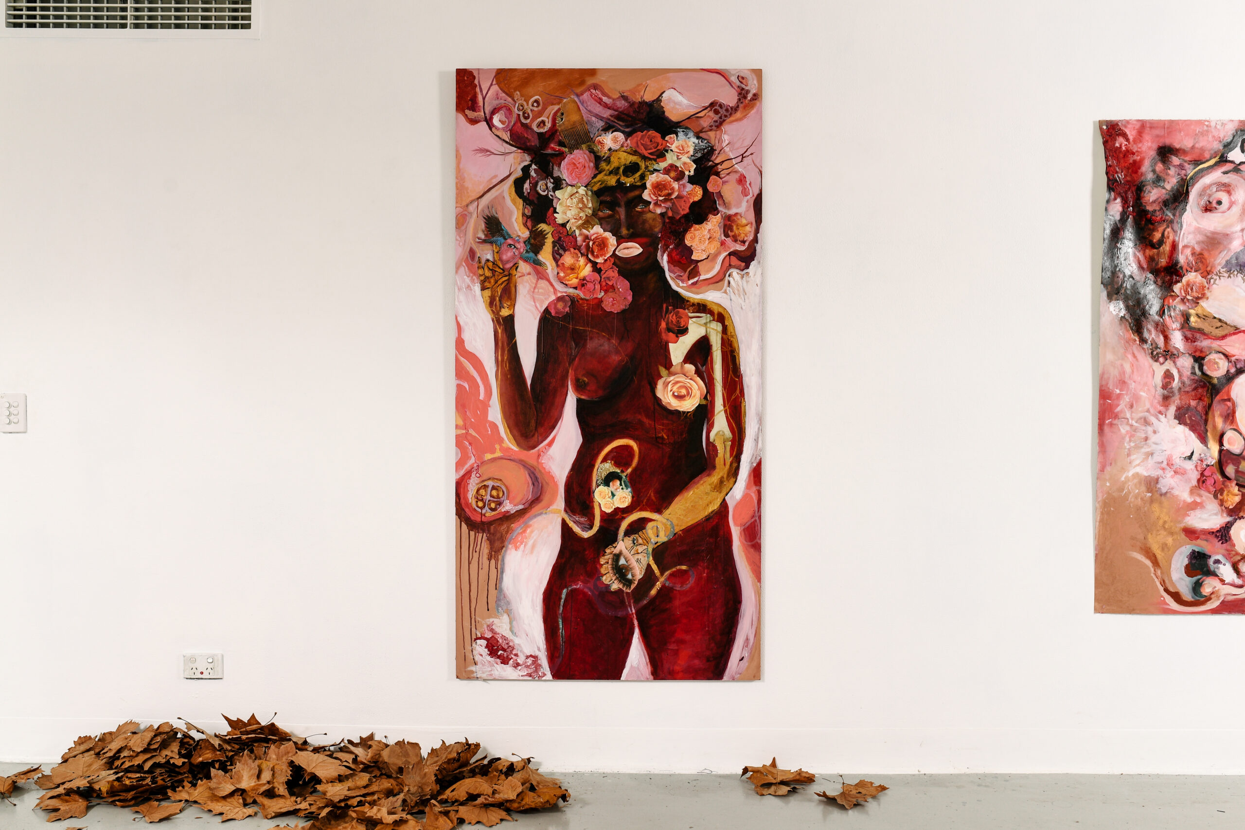 A large unframed painting of a naked black person surrounded by a flower head garland of reds, pinks, beige and rose colours.