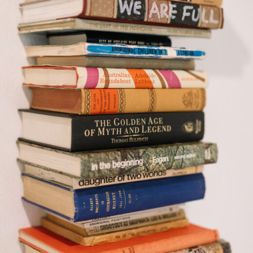 Detail of a sculpture of a tall stack of books, spines facing us with various titles.