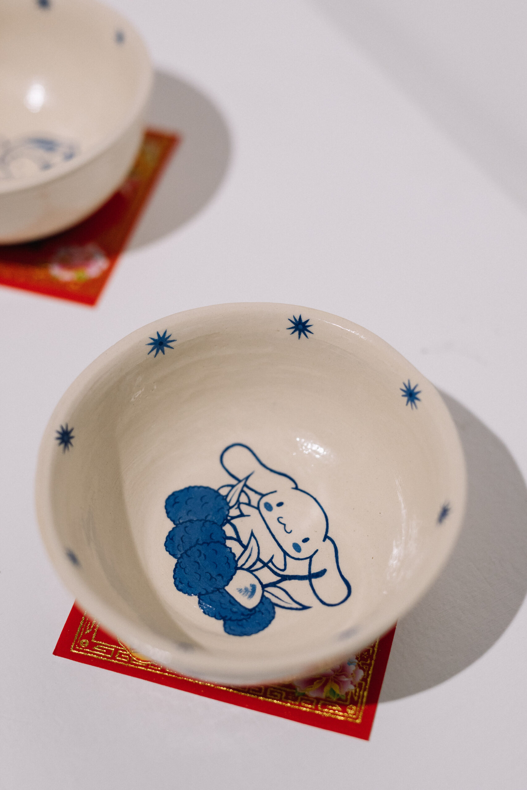 Detail of a cream ceramic with a blue glaze line drawing of a cartoon creature.