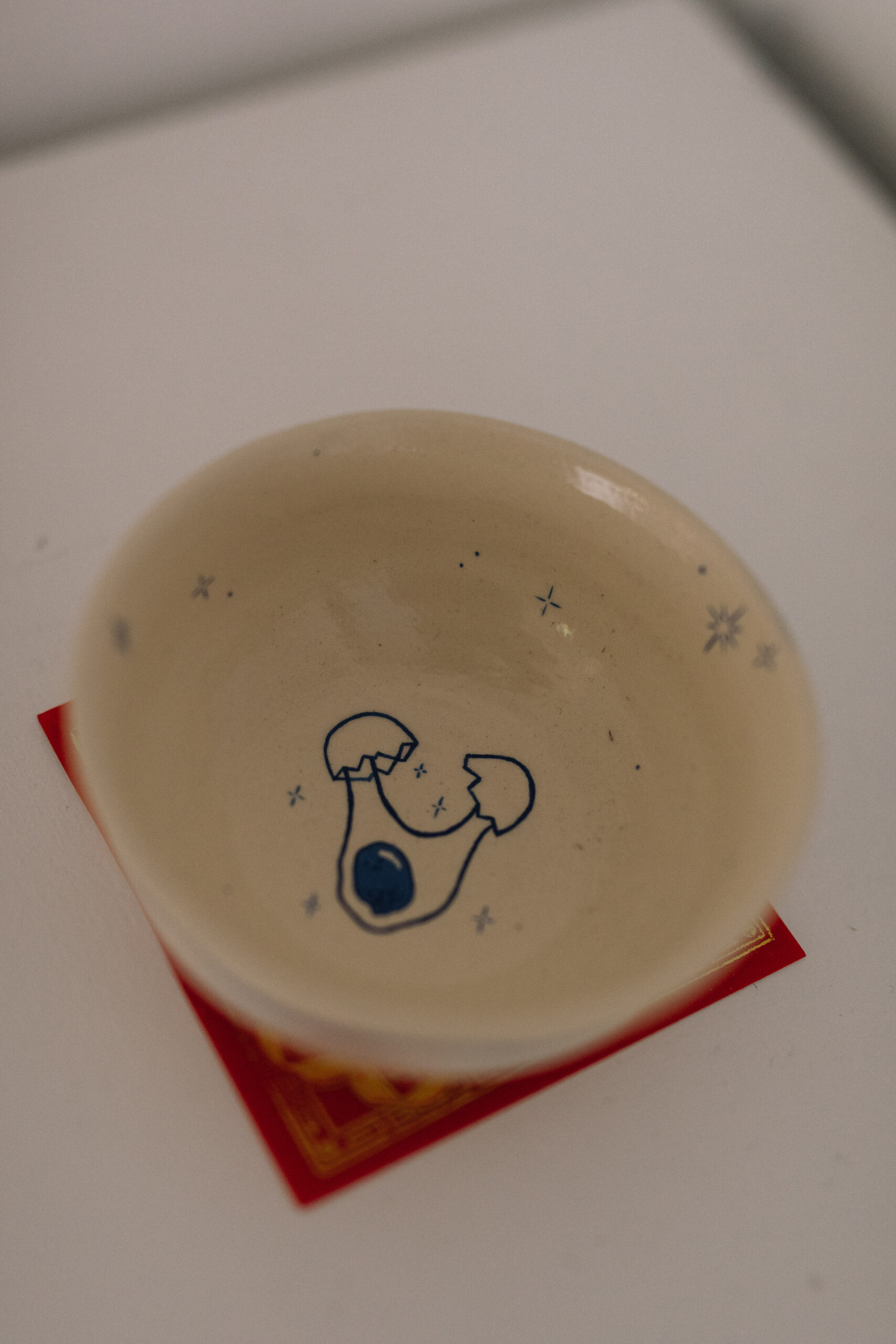 Detail of a ceramic with a blue line drawing of a cracked egg.