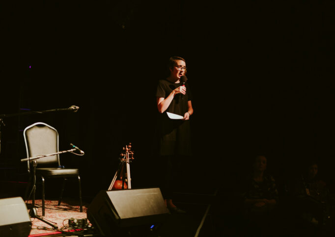 CEO and Artistic Director Emily Tulloch standing on stage and speaking into a microphone.