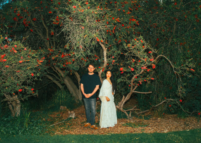 Flash photograph taken at night of composers Mindy Meng Wang and Tim Shiel stand posed against a red wattle tree.