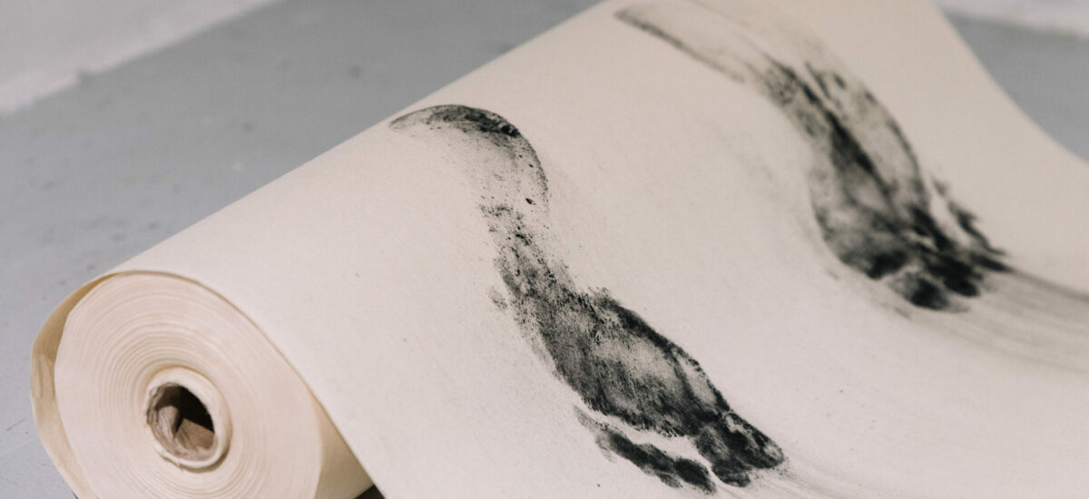 A roll of rice paper laying on the ground with charcoal feet impressions printed on the surface