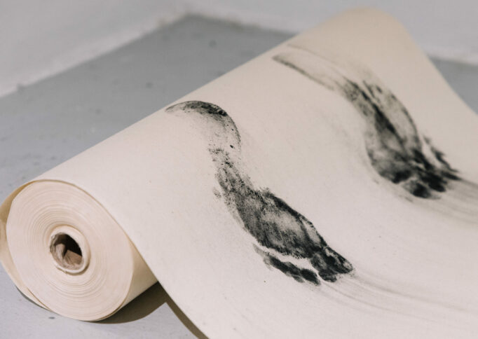 A roll of rice paper laying on the ground with charcoal feet impressions printed on the surface
