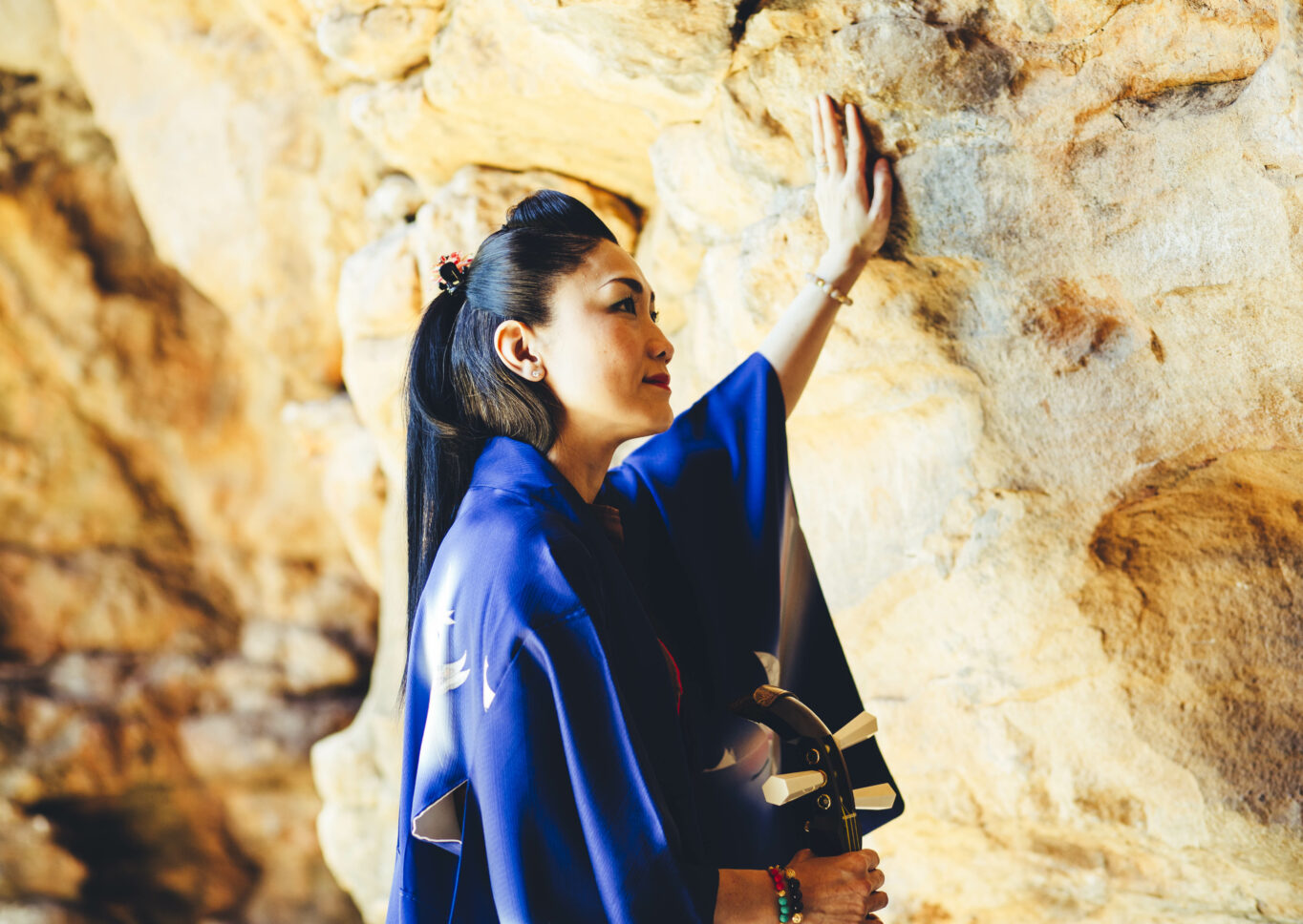Photo of woman standing inside a cave with one had resting against cave wall