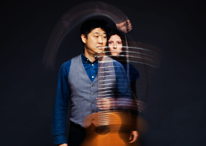 Photo of a man and woman holding a guitar and violin bow
